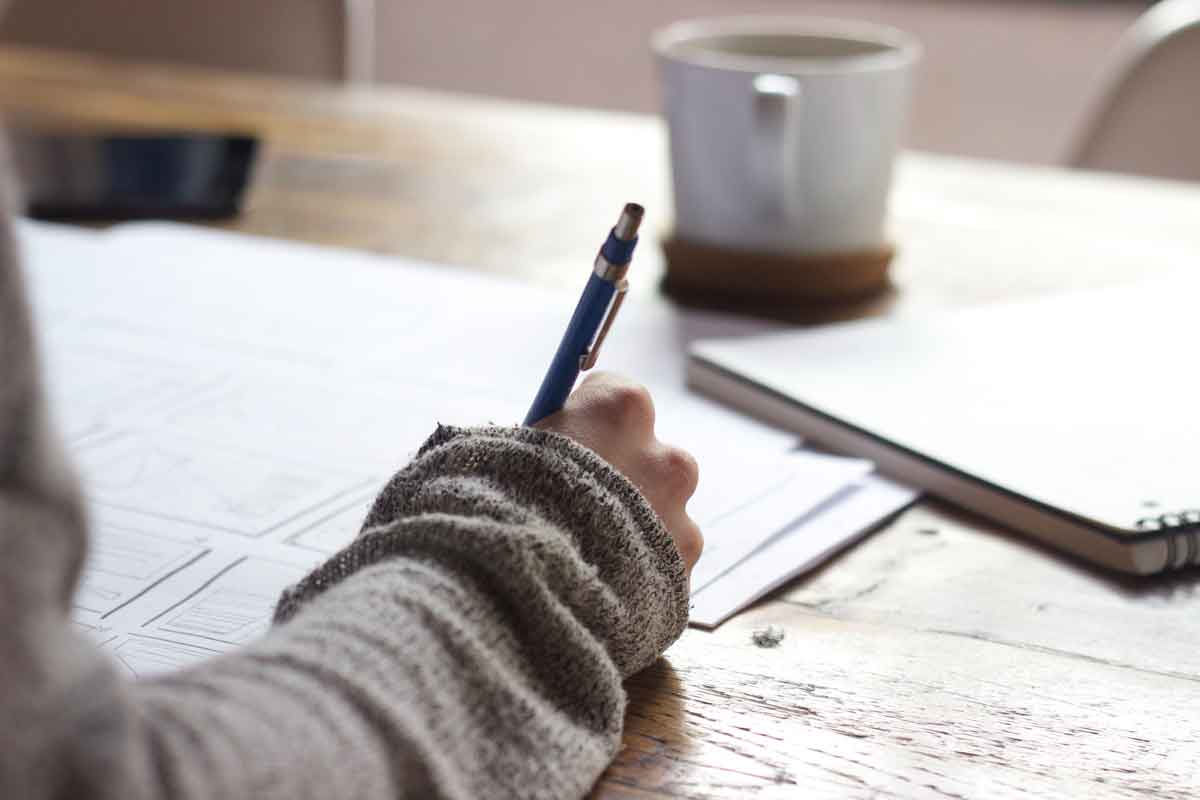 Student hand holding a pen while looking at papers on a desk